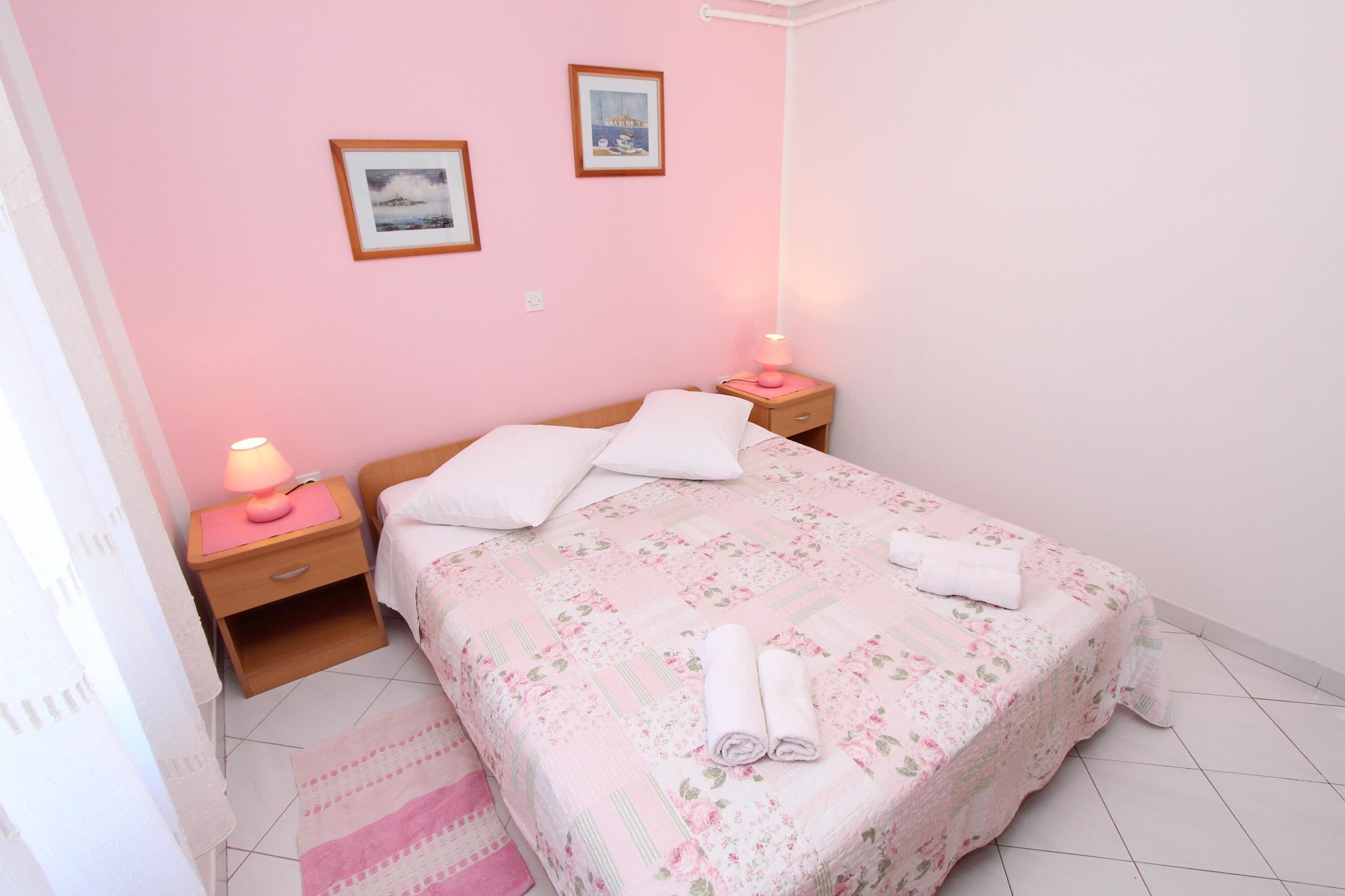 Een slaapkamer met een bed, twee nachtkastjes en een roze muur.
