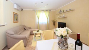 A living room with a beige sofa, a small table with a vase of flowers, and a bottle of wine on a white table.