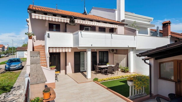 A two-story house with a patio, a car parked outside, and a small garden.