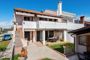 Une maison à deux étages avec un patio, une voiture garée devant et un petit jardin.