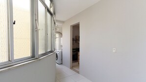 A hallway with a washing machine, a window, and a kitchen area visible through an open door. - Rio Spot Homes D050 (Rio de Janeiro)