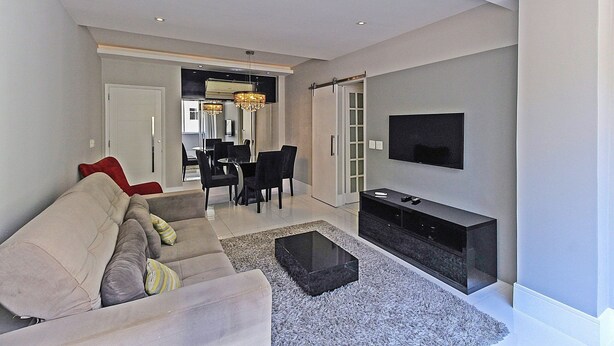 A modern living room with a sofa, a coffee table, a TV, and a dining area with chairs and a table. - Rio Spot Homes D050 (Rio de Janeiro)