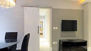 A modern living room with a glass dining table, black chairs, a flat-screen TV mounted on the wall, and a sliding door leading to another room. - Rio Spot Homes D050 (Rio de Janeiro)