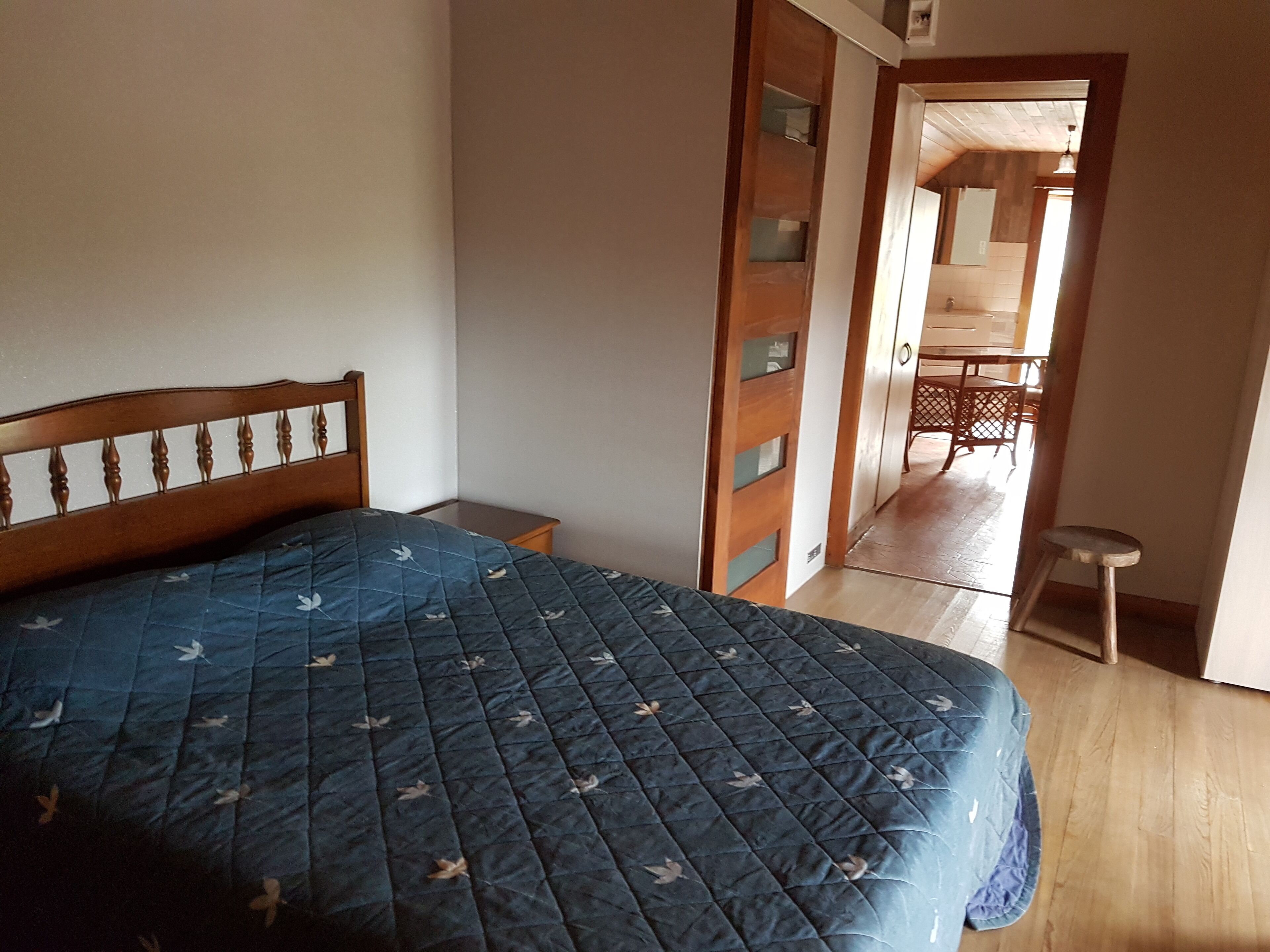 Una camera da letto con un letto, un armadio in legno, uno sgabello e una porta che dà su un balcone.