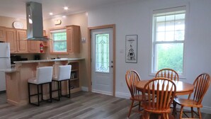 A modern kitchen with wooden cabinets, a built-in stove, and a dining area with a round table and wooden chairs. - New! Fabulous Farmhouse (Cape Dauphin)