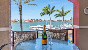 Mesa com garrafa e copos, com vista para uma marina com barcos e palmeiras.