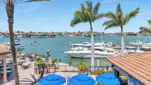 Marina com barcos atracados, área de café com mesas ao ar livre e vista clara da água.