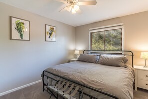 Een slaapkamer met een bed, een nachtkastje, een lamp, een plafondventilator en twee ingelijste foto's aan de muur.