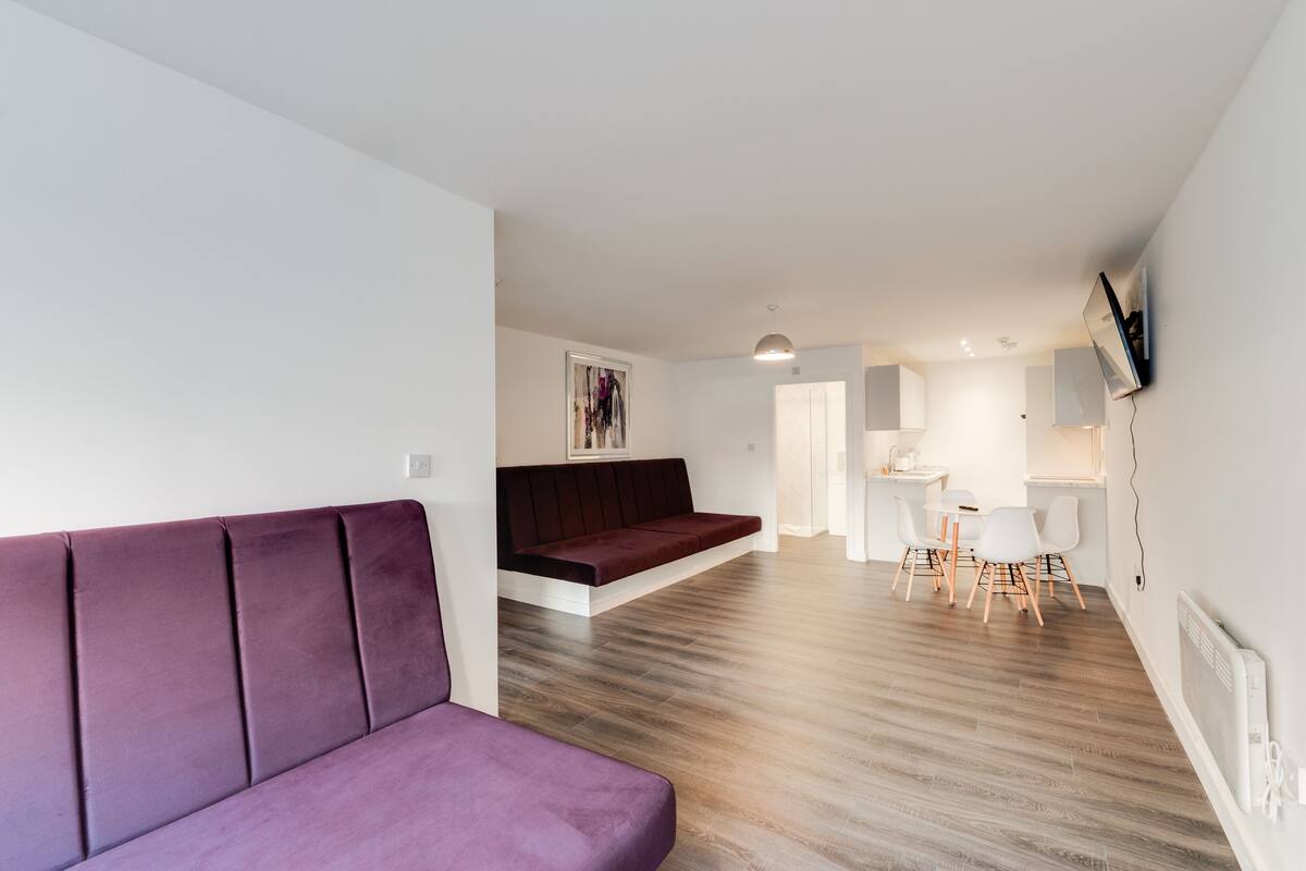 A modern living room with a purple sofa, a dark red bench, and a dining area with a small table and chairs.