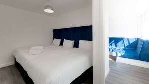 A modern hotel room with a large bed, a dark blue headboard, and a view of a blue outdoor seating area. - iStay Liverpool Bold Street (Liverpool)