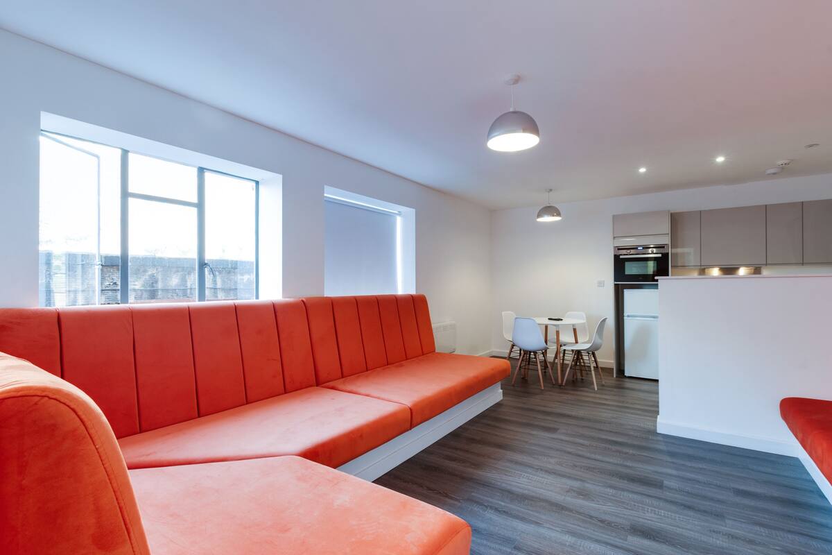 A modern living space with a sofa, dining table, chairs, and a kitchen area.
