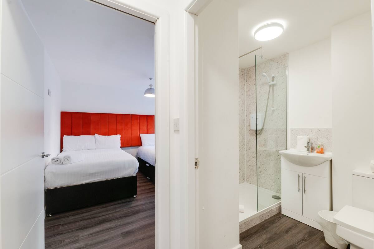 A modern hotel room with a red headboard, a separate shower area, and a white sink.