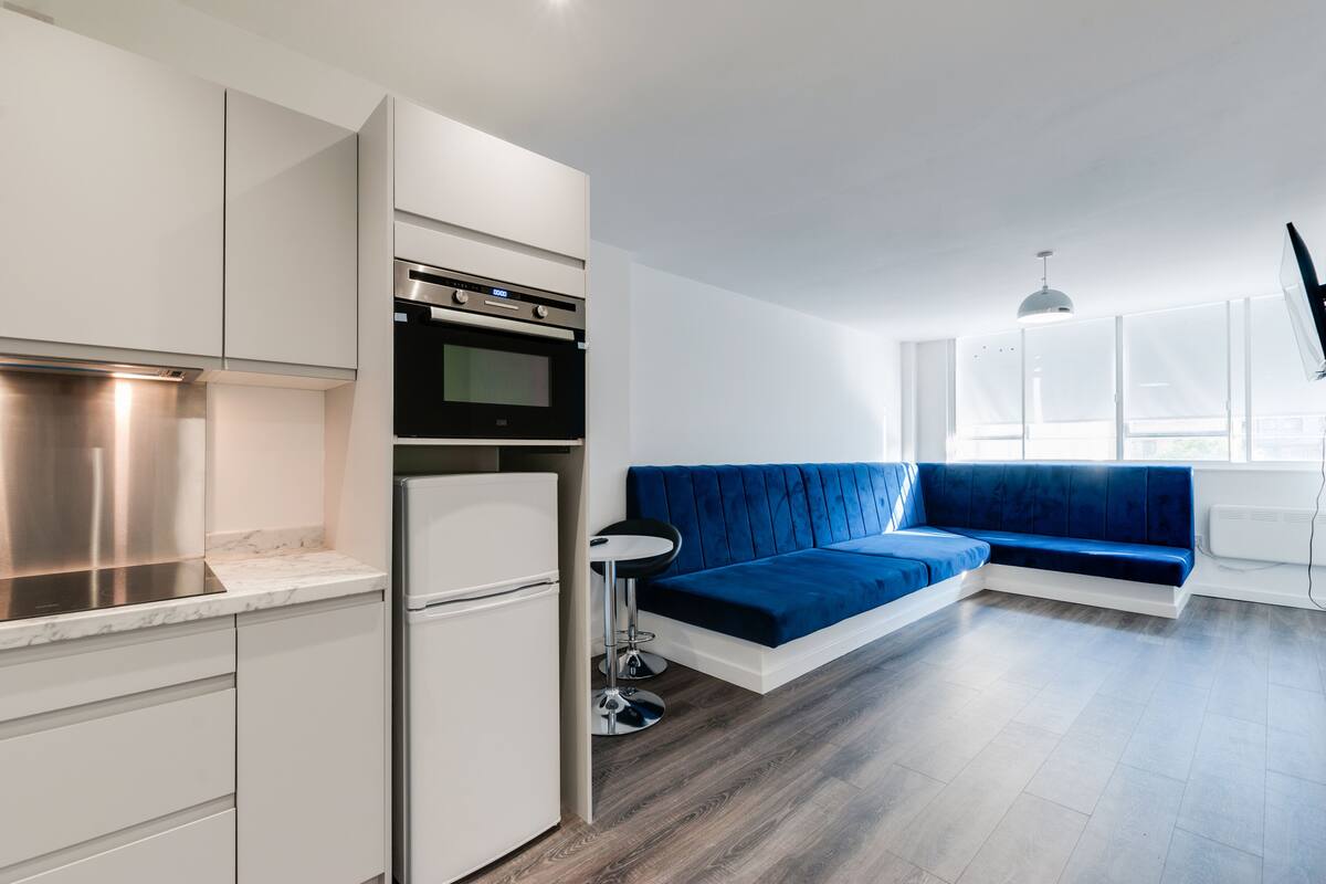 A modern kitchen with built-in appliances, a seating area with a blue sofa, and large windows providing natural light.