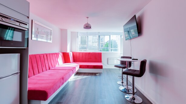 A modern living room with a red sofa, a dining area with a table and chairs, a built-in oven, and a TV mounted on the wall. - iStay Liverpool Bold Street (Liverpool)