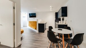 A modern kitchen with a built-in island, a dining area with a white table and black chairs, and a yellow sofa in the background. - iStay Liverpool Bold Street (Liverpool)