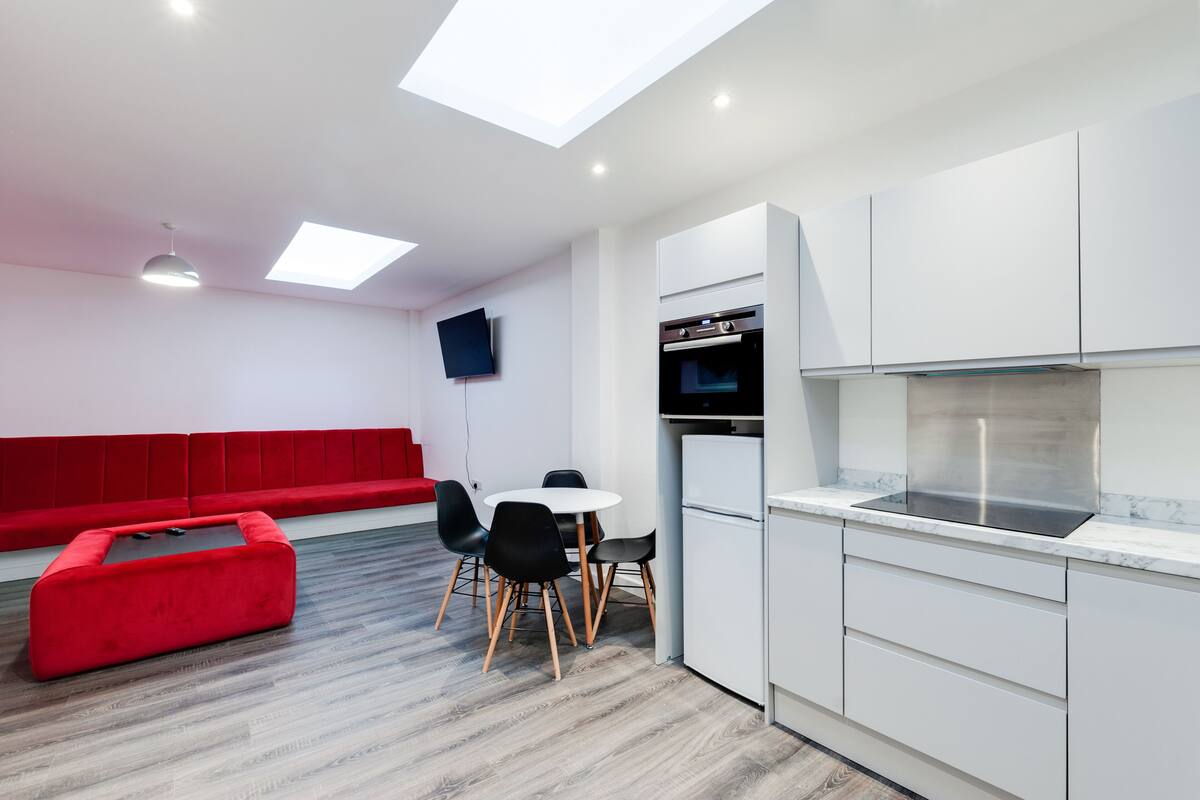 A modern kitchen with white cabinets, a built-in oven, and a dining area with a red bench and black chairs.