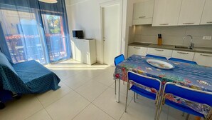 Una habitación con mesa de comedor, sillas, televisor, kitchenette y puerta corrediza de vidrio que da a un espacio exterior.