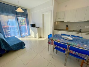 Una habitación con mesa de comedor, sillas, televisor, kitchenette y puerta corrediza de vidrio que da a un espacio exterior.