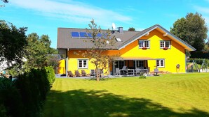 A yellow house with a sloped roof, solar panels, and a well-maintained lawn.