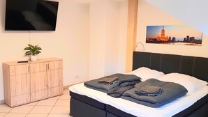 A bedroom with a bed, a TV mounted on the wall, a cabinet, and a cityscape picture.