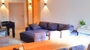 A modern living room with a grey sofa, wooden coffee table, and a white desk with a plant.