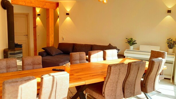 A cozy living room with a wooden dining table, comfortable seating, a fireplace, and a staircase.