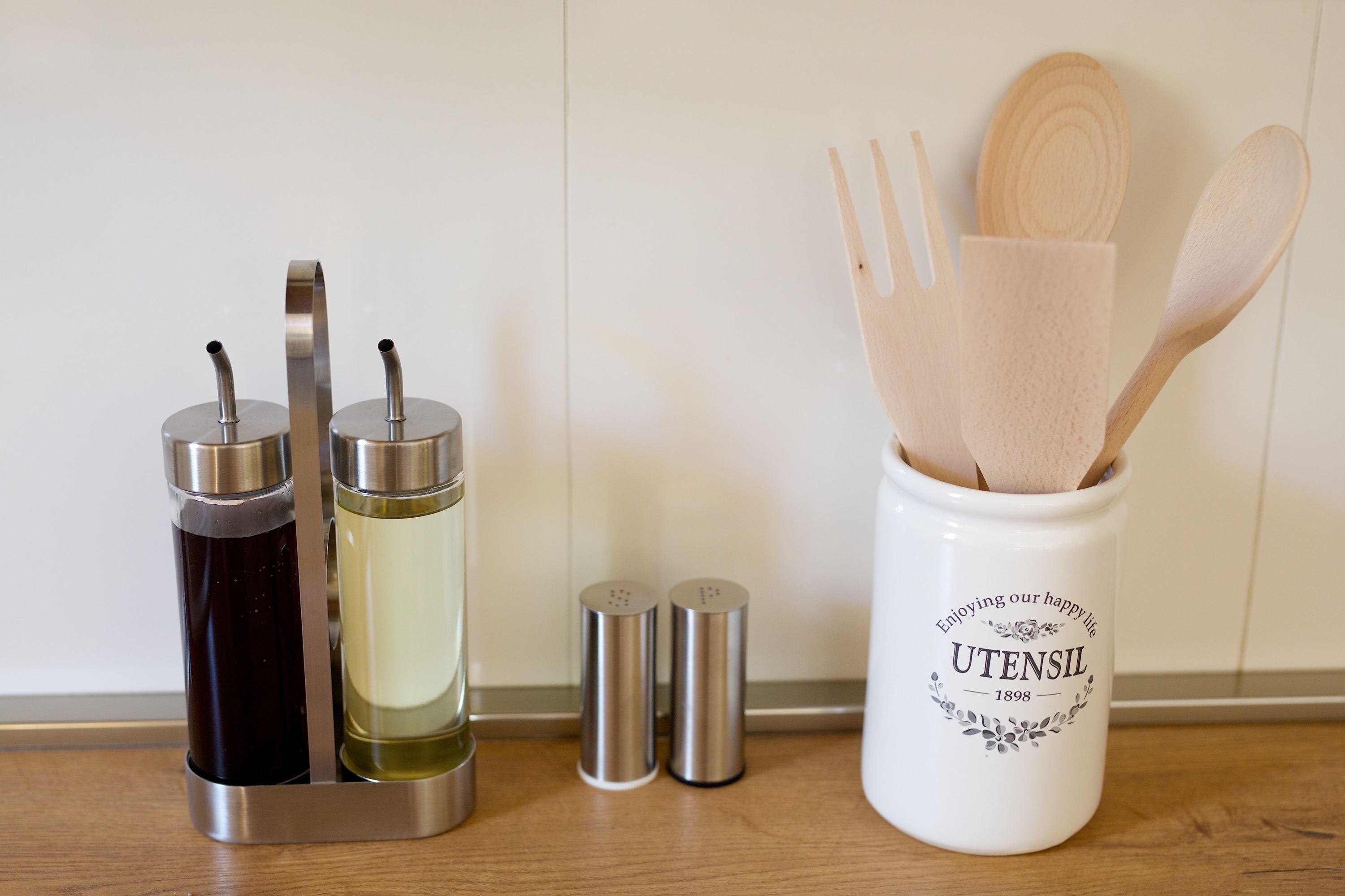 A kitchen utensil holder with wooden spoons and a white mug labeled 'UTENSIL' on a wooden countertop.