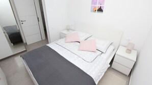 A bedroom with a bed, two bedside tables, a nightstand, a mirror, and a wall-mounted picture. - Apartments Polenta (Rovinj)