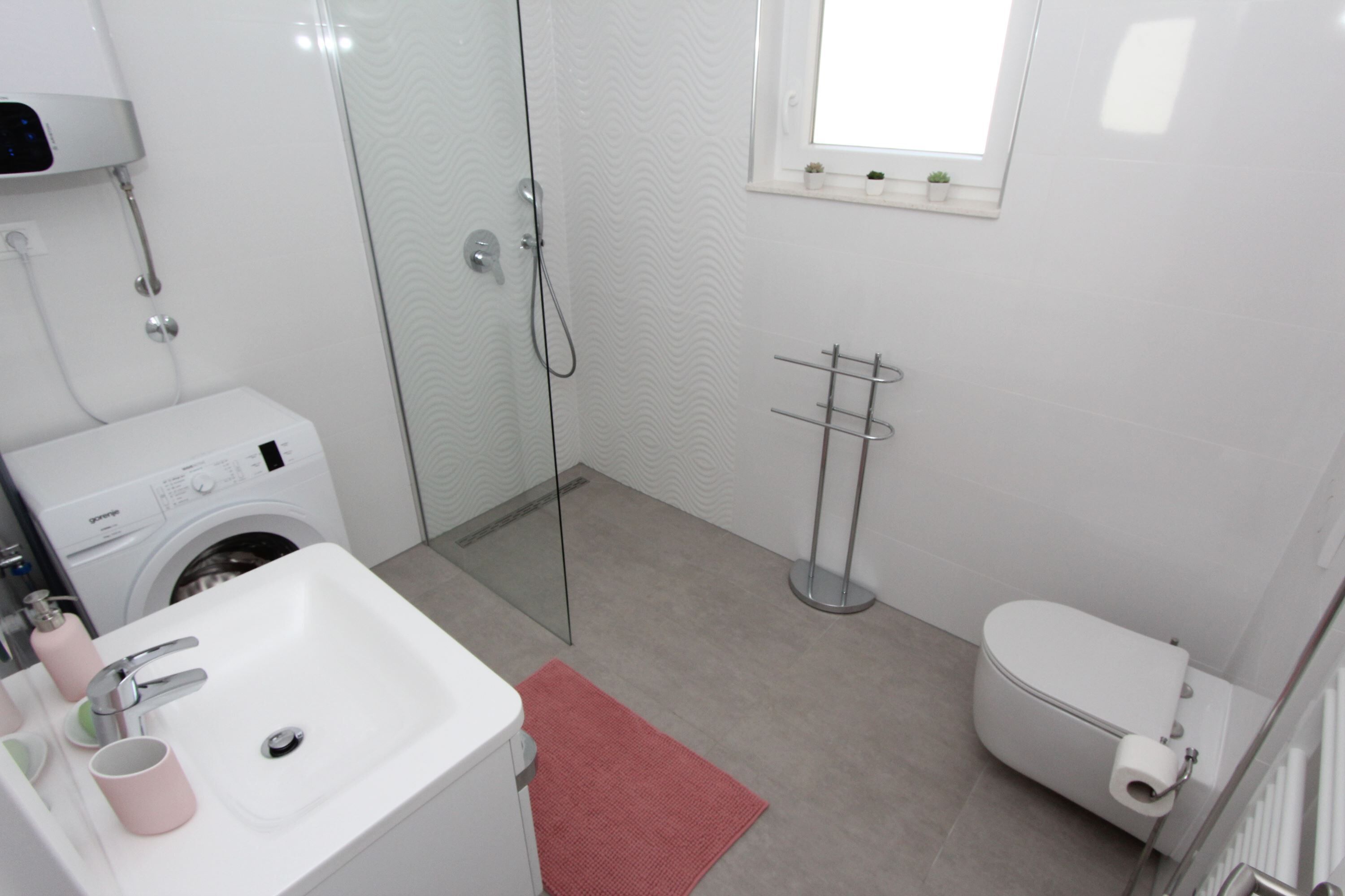 A modern bathroom with a washing machine, a sink, a glass shower enclosure, and a toilet.