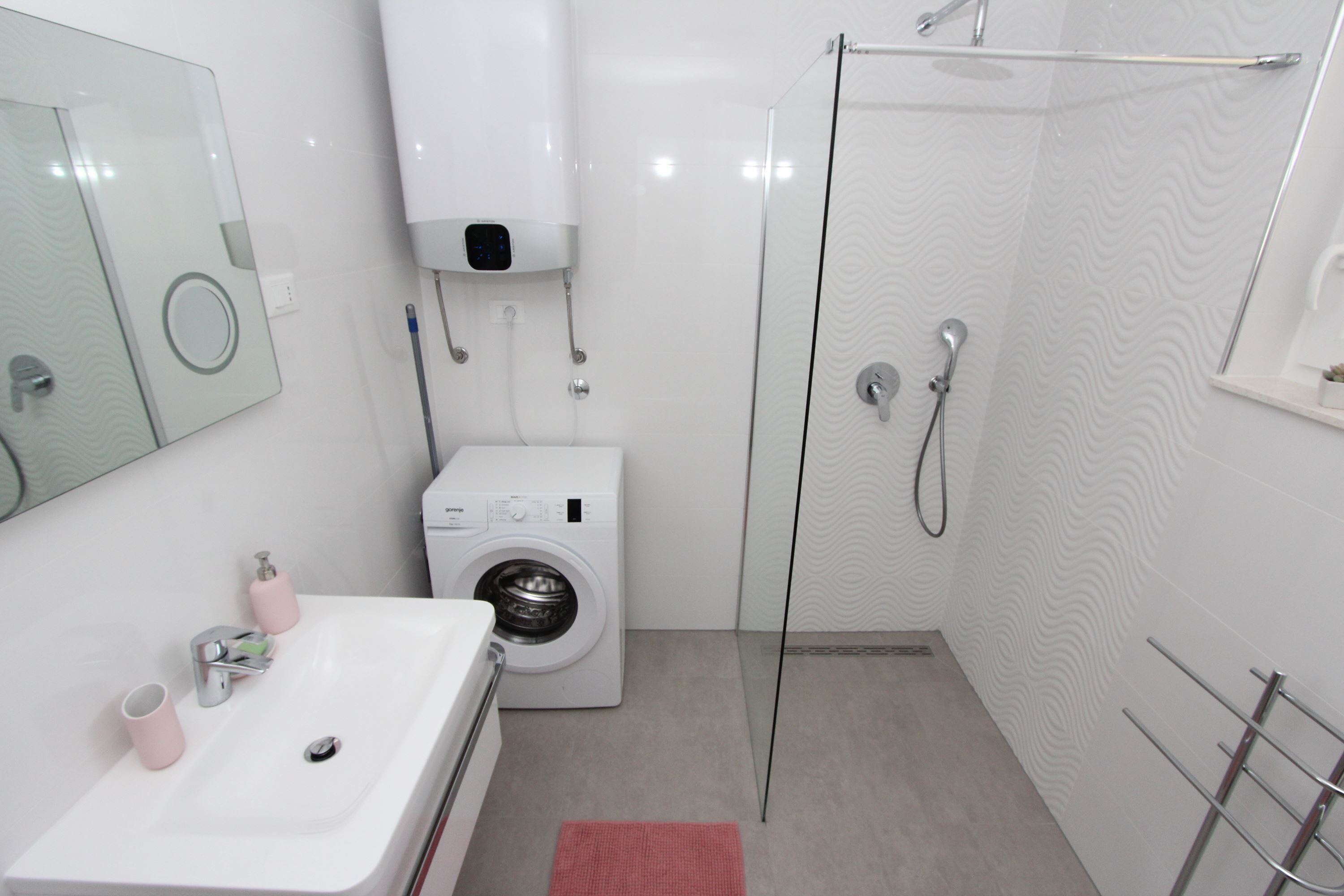 Une salle de bain moderne avec un lavabo blanc, un lave-linge, une cabine de douche en verre et un porte-serviettes.