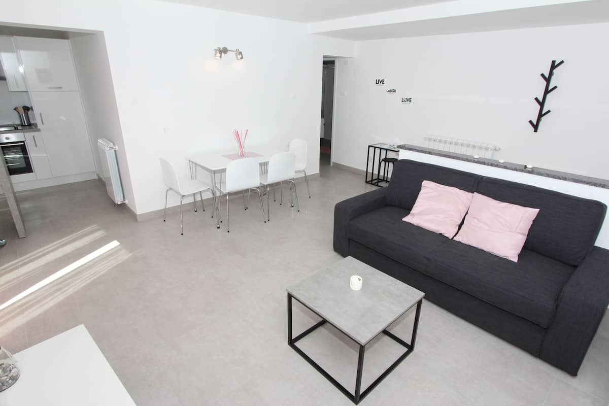 A modern living room with a grey sofa, a small coffee table, and a dining area with white chairs and a table.