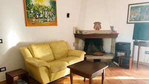 A living room with a yellow sofa, a wooden coffee table, a fireplace, and a television on a wooden stand.