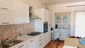 A kitchen with white cabinets, a gas stove, a sink, and a dining area with a table and chairs.