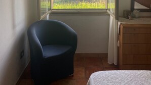 A room with a large window, a chair, a bed, and a dresser.