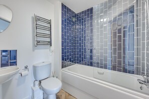 Ein Badezimmer mit Toilette, Waschbecken, Badewanne und einer Duschkabine mit blauen Fliesen.