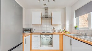 A compact kitchen with white cabinets, a stainless steel oven, and a microwave. - City Centre Flat - Free Parking, Wifi & SmartTV (Milton Keynes)