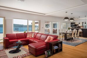 Una sala de estar moderna con un sofá de cuero rojo, una mesa de centro de vidrio y un comedor con una cocina al fondo.