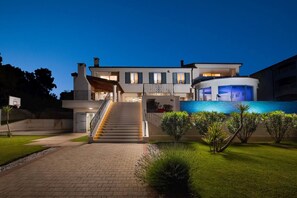 Una casa moderna de dos pisos con piscina, una escalera que conduce a la entrada y un césped bien cuidado.