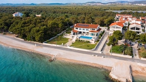An aerial view of a coastal property with a swimming pool, multiple buildings, and a beach.