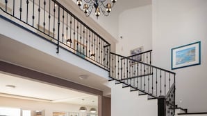 A spacious living area with a staircase, a chandelier, and a view of the outdoors.