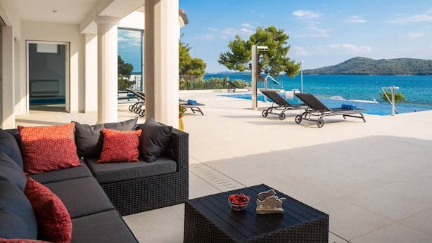 A modern outdoor seating area with a pool, lounge chairs, and a view of the sea.