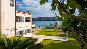 A modern building with a balcony overlooking a lake, a well-maintained lawn, and a clear sky.