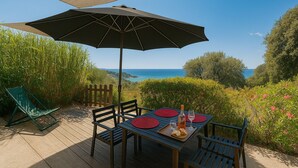 A deck with a table set for two, a large umbrella, and a view of the sea. - Apartment **** sea view in the heart of the Corsican maquis, 5 mm from the beach (Cargèse)