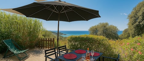 Een terras met een tafel voor twee, een grote parasol en uitzicht op zee.