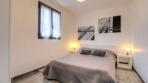 A bedroom with a bed, two bedside tables with lamps, a window with curtains, and two wall-mounted artworks. - Apartment **** sea view in the heart of the Corsican maquis, 5 mm from the beach (Cargèse)