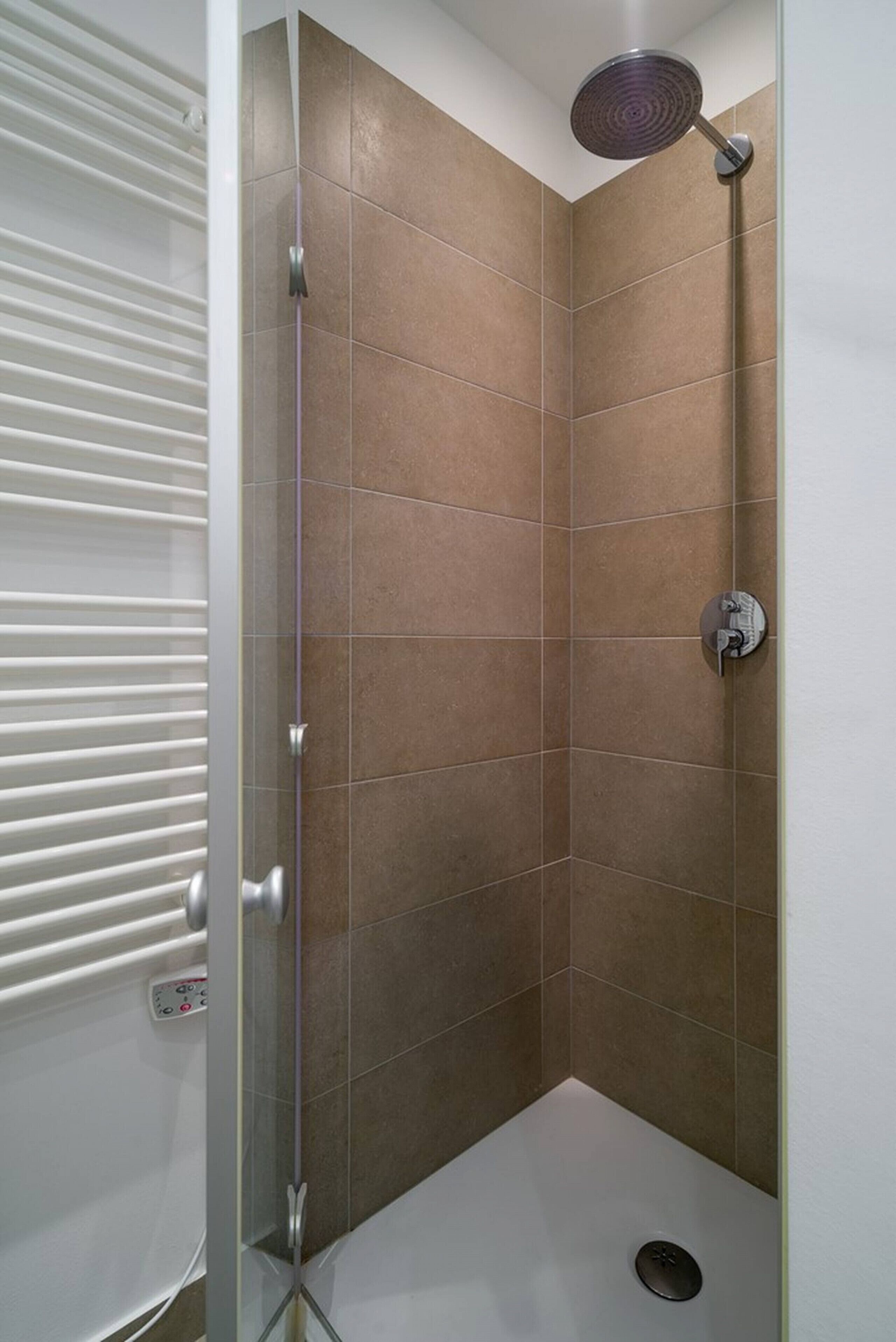 Een douche met een handdouche, een betegeld hoekdesign en een bedieningspaneel aan de muur.