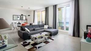 A modern living room with a sectional sofa, a glass coffee table, and a dining area with a white table and chairs.
