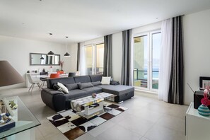 A modern living room with a sectional sofa, a glass coffee table, and a dining area with a white table and chairs.