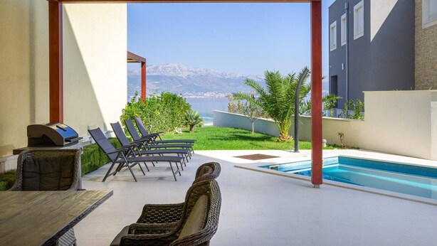 A covered outdoor area with a pool, lounge chairs, and a grill.