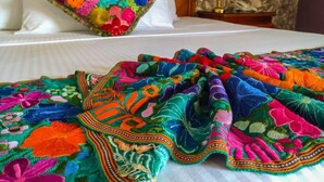 Una cama con un colorido edredón bordado y una almohada decorativa.